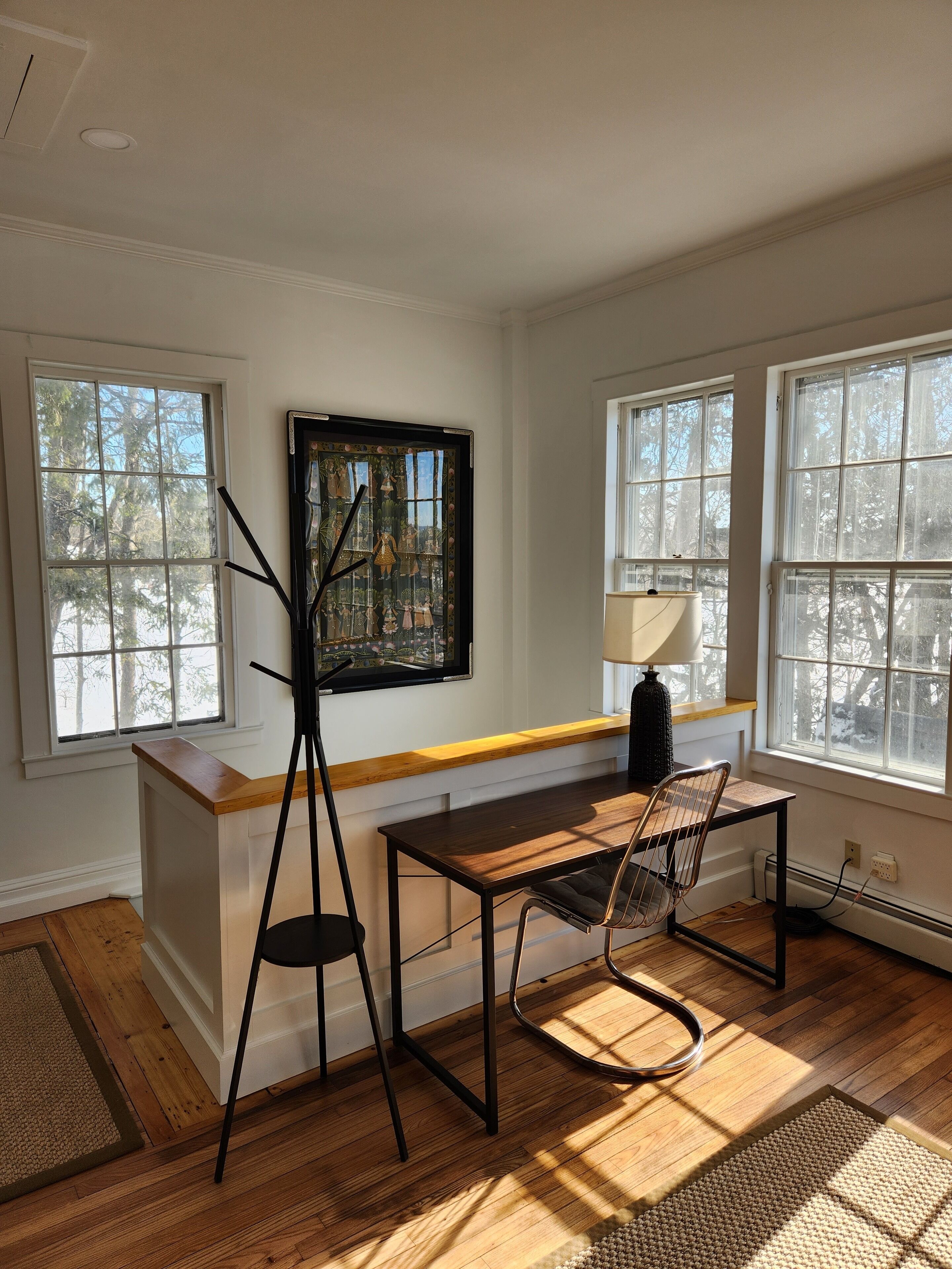 A room with a wooden desk, a chair, a floor lamp, and a painting on the wall.