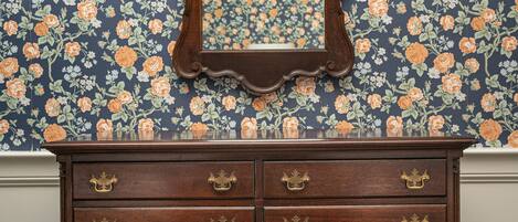 A wooden dresser with ornate carvings and brass handles against a floral wallpaper background.