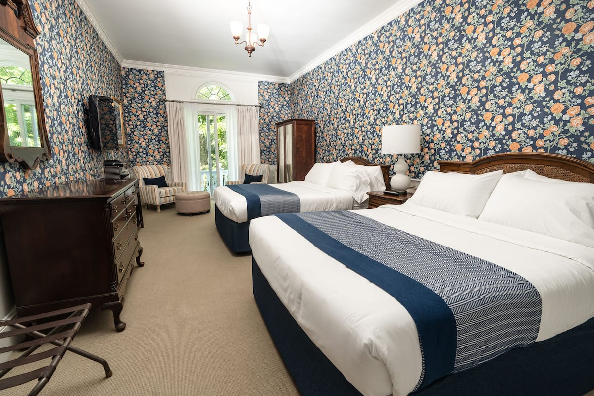 A hotel room with two beds, a dresser, a chair, a mirror, and a window with curtains.