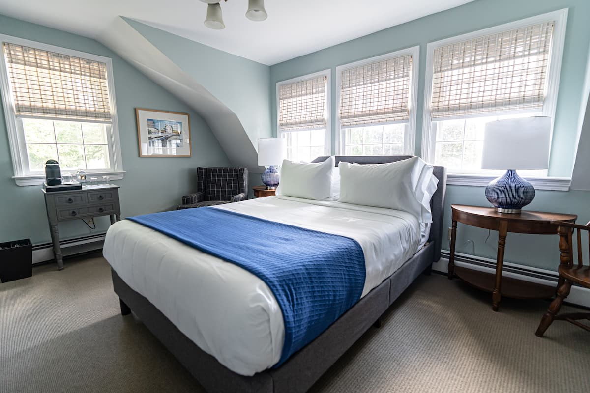 A bedroom with a large bed, a nightstand, a dresser, and a window with blinds.