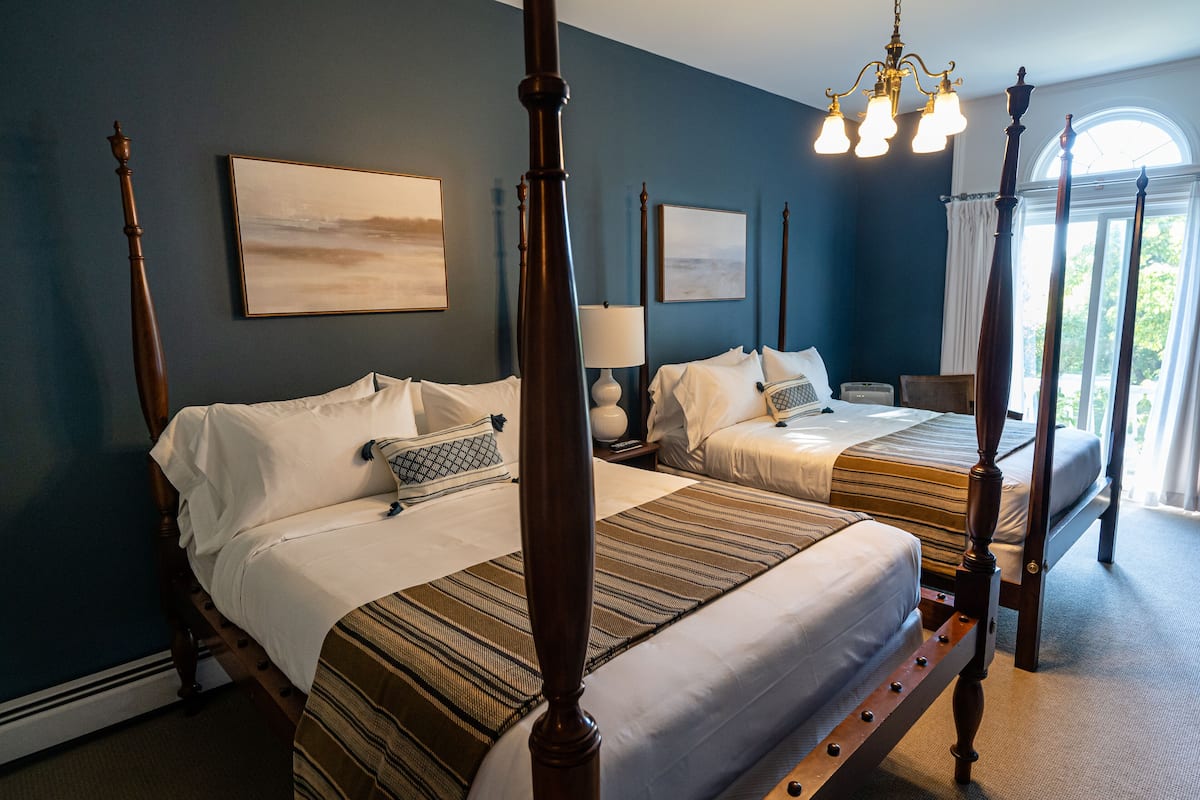 A four-poster bed with a wooden frame, two bedside tables with lamps, and two paintings on the wall.