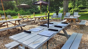 A series of picnic tables with "RESERVED" signs, surrounded by Adirondack chairs and umbrellas in a wooded park setting.