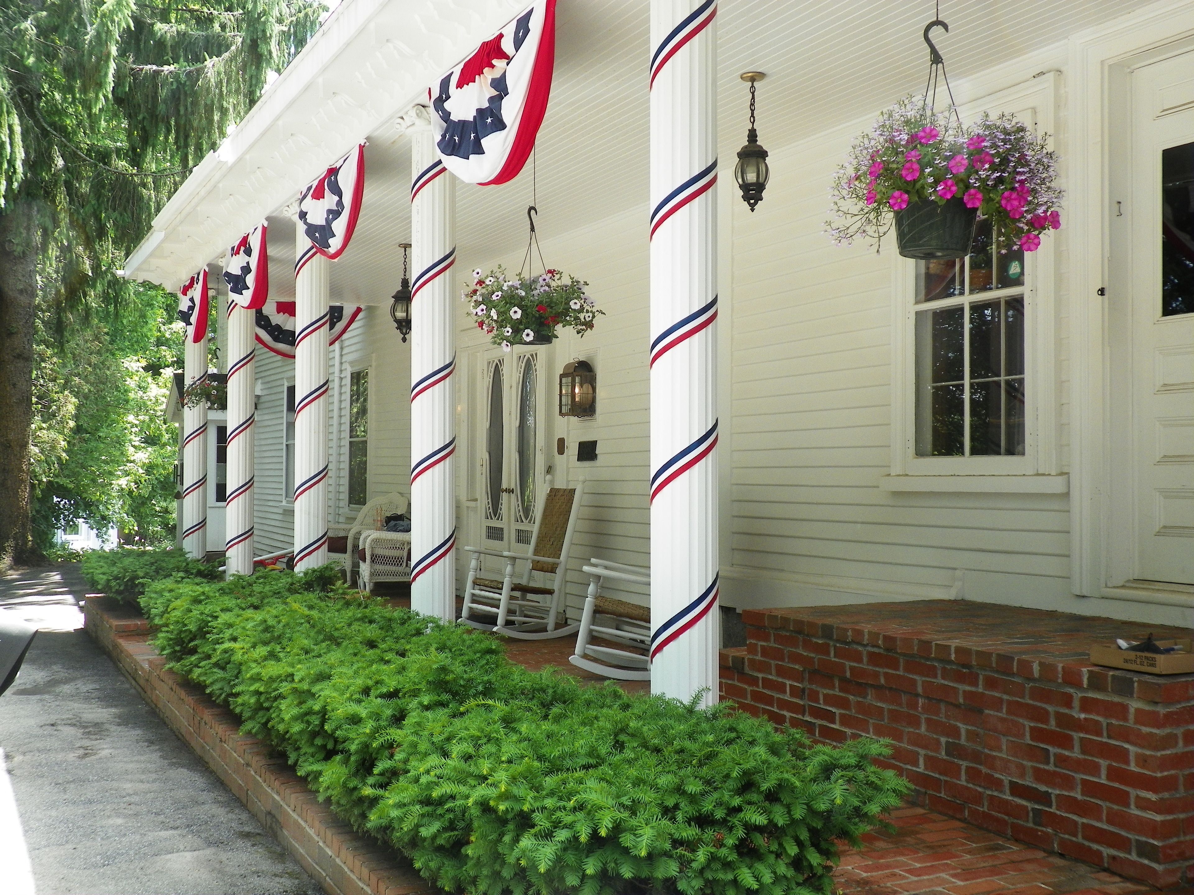 A white building with red and blue striped columns, a brick porch, and hanging flower baskets.