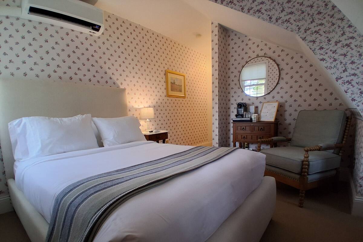 A neatly made bed with a striped blanket, a wooden chair, a nightstand with a lamp, and a dresser with a mirror.