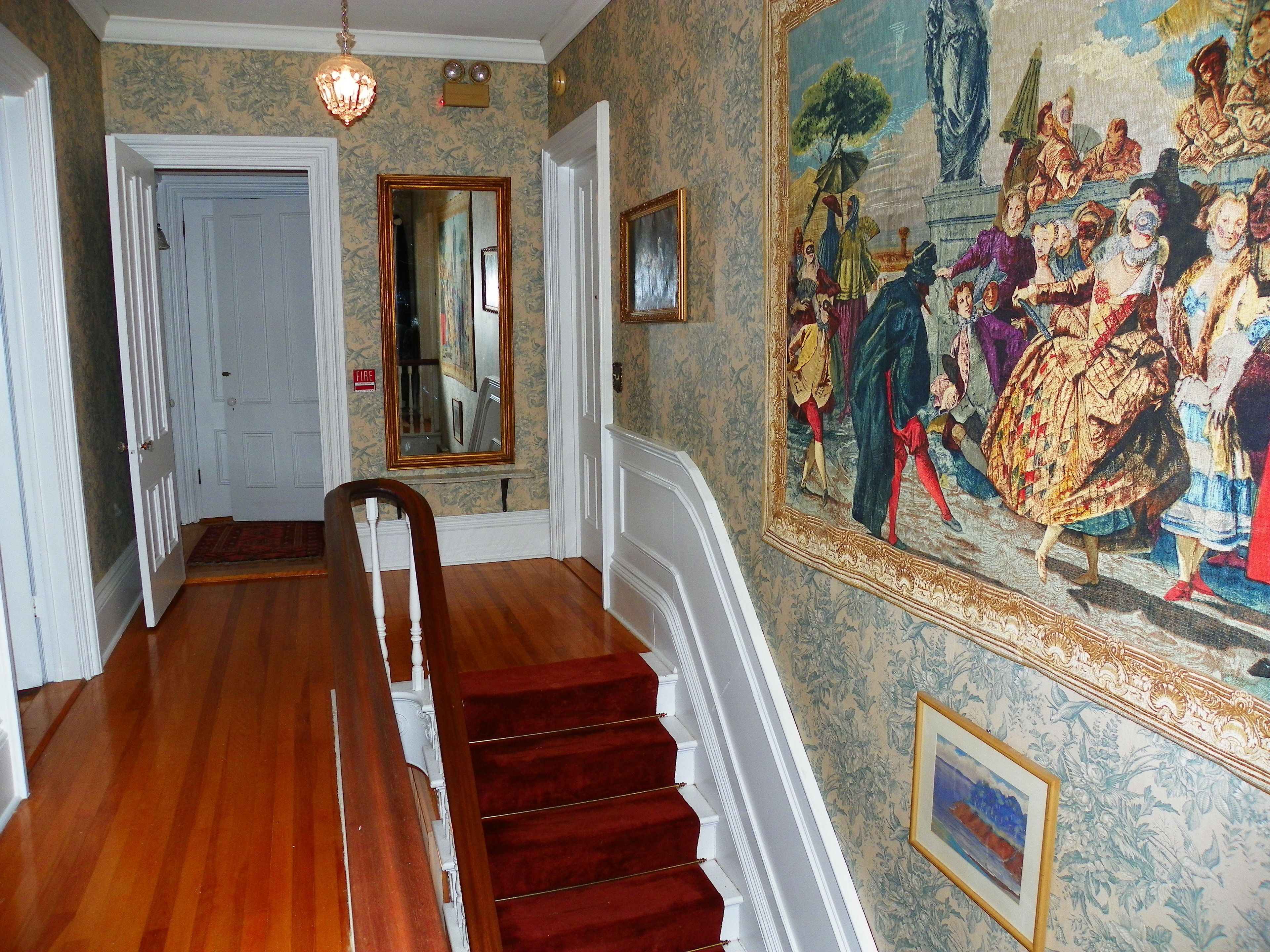 Un magnifique escalier en colimaçon avec une rampe en bois, une moquette rouge et un grand tableau décoratif accroché au mur.