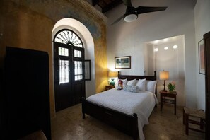 A hotel room with a bed, a desk, a chair, a door with a window, and a ceiling fan. - Casa Sol Bed and Breakfast (San Juan)