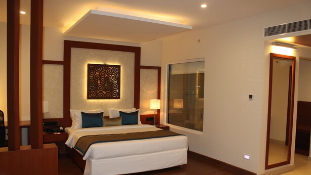 A hotel room with a large bed, a bedside table, a nightstand, a window, and a door. - The Altruist Hitech Hotel (Hyderabad)