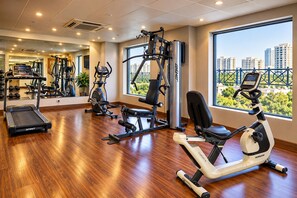 A gym with various exercise equipment, a treadmill, and a view of buildings through large windows. - The Altruist Hitech Hotel (Hyderabad)