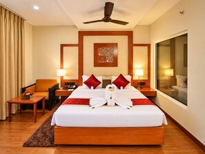A hotel room with a large bed, two bedside tables, a desk, a chair, a ceiling fan, and a large window. - The Altruist Hitech Hotel (Hyderabad)