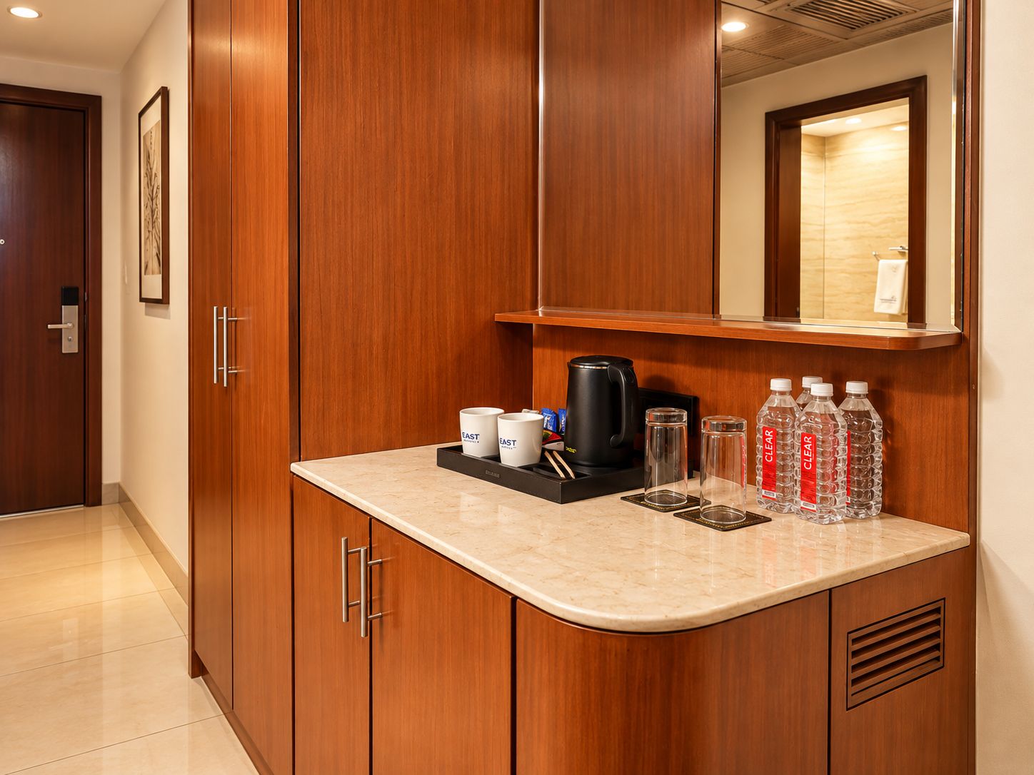 A hotel room with a wooden cabinet, a countertop with a coffee maker, cups, glasses, and water bottles.