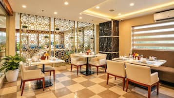 A restaurant with checkered flooring, white tables, and chairs, and a decorative partition with plants.