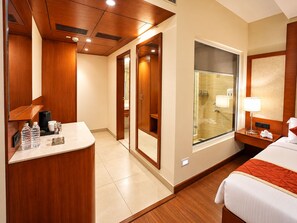 A hotel room with a bed, a bedside table with a lamp, a bathroom with a glass shower enclosure, and a wooden vanity with a mirror. - The Altruist Hitech Hotel (Hyderabad)