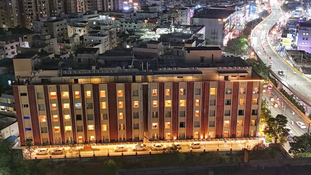 A multi-story hotel with a row of rooms, a parking area, and a busy street in the background. - The Altruist Hitech Hotel (Hyderabad)
