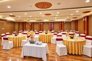 A conference room with round tables, white chairs with red sashes, and a projector on a table. - The Altruist Hitech Hotel (Hyderabad)
