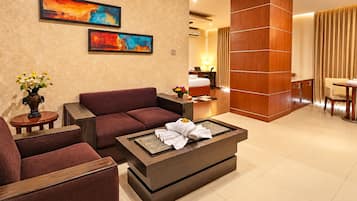 A modern hotel room with a sofa, a coffee table with towels, a desk, and a bed.