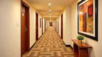 A hotel hallway with wooden doors, a patterned carpet, recessed lighting, and a framed abstract painting.