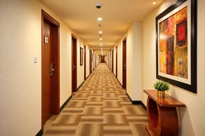 Un couloir d’hôtel avec des portes en bois, une moquette à motifs, un éclairage encastré et un tableau abstrait encadré.