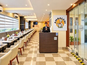 A hotel lobby with a reception desk, a long dining area with tables and chairs, and a wall with a restaurant sign. - The Altruist Hitech Hotel (Hyderabad)