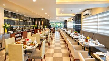 A hotel restaurant with a long dining area, buffet, and a view of the outdoors.