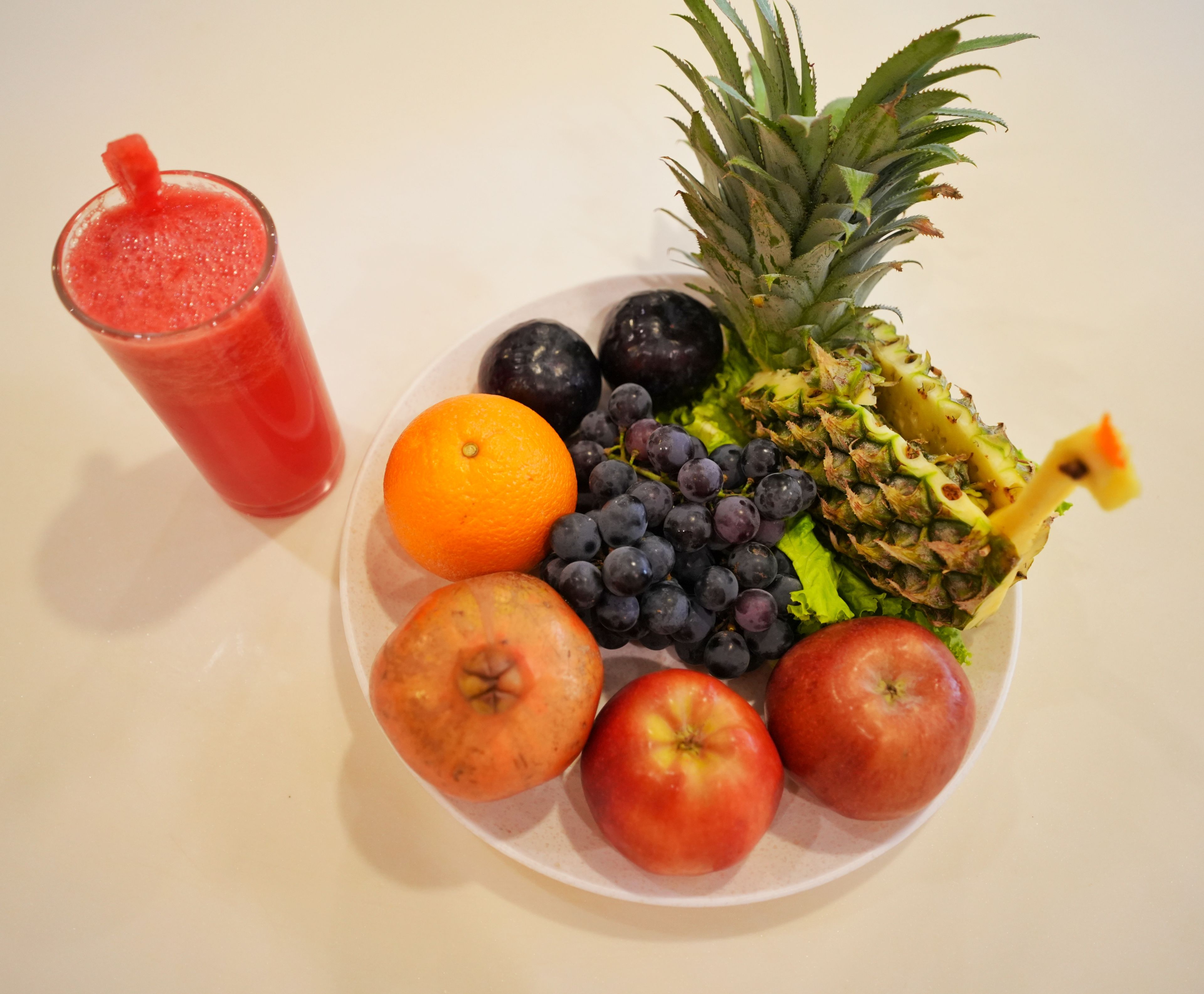 A plate of fruits and a glass of red drink on a table.