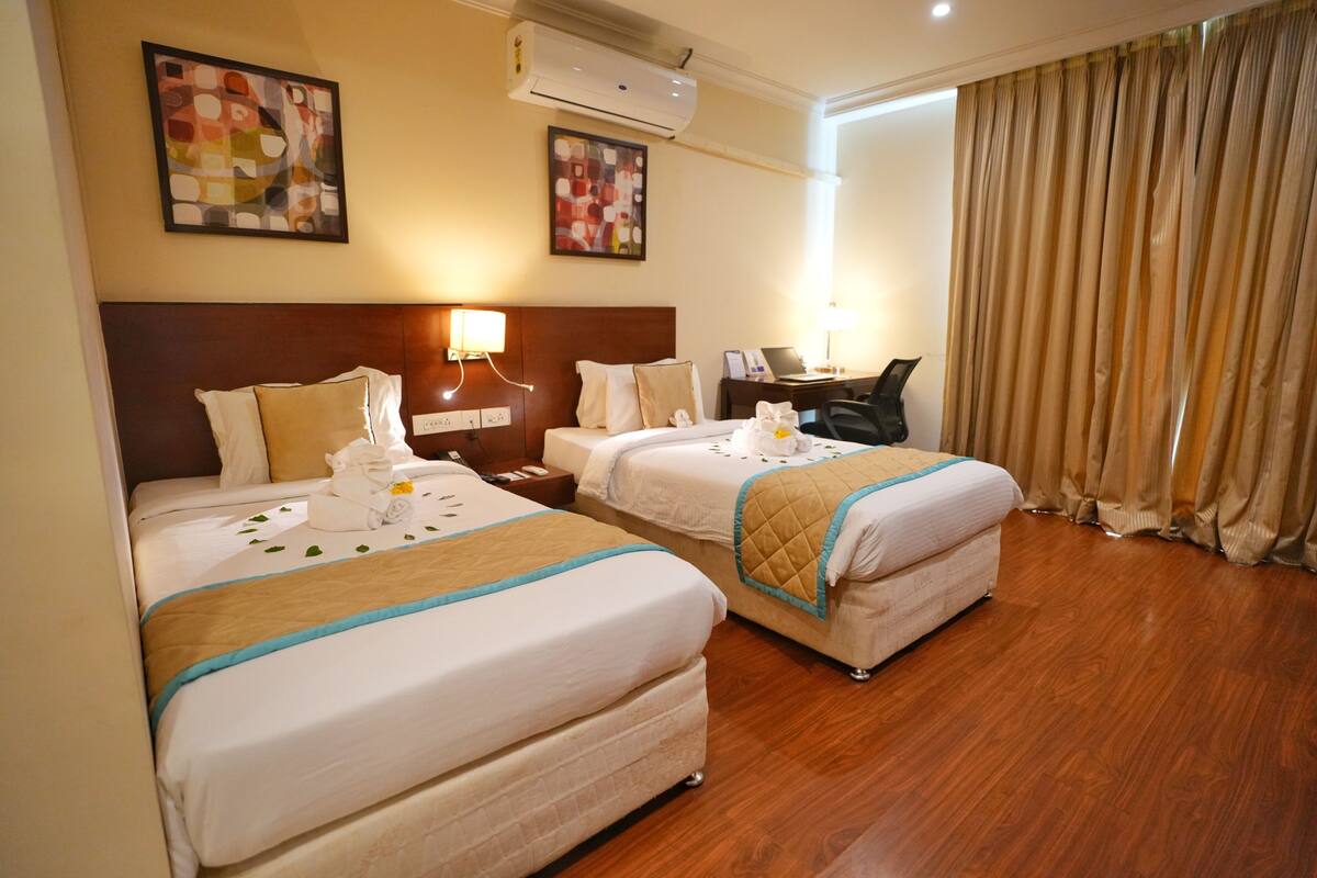 A hotel room with two beds, a desk, a chair, and an air conditioning unit.
