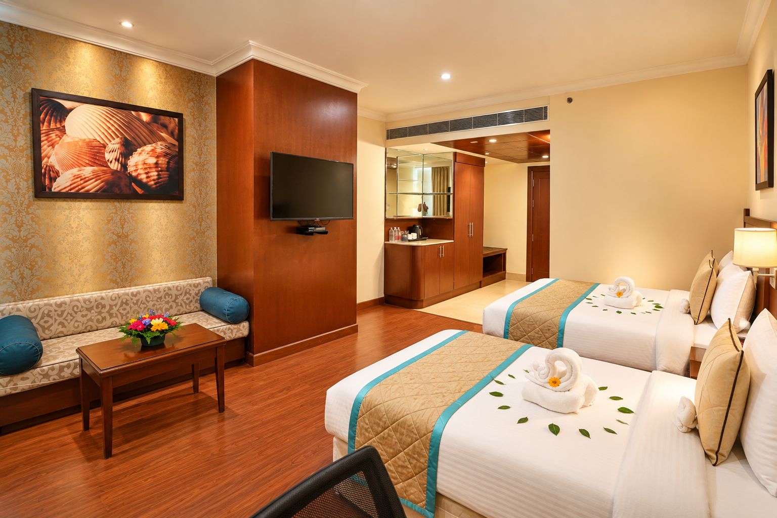 A hotel room with two beds, a sofa, a TV, and a dining area.