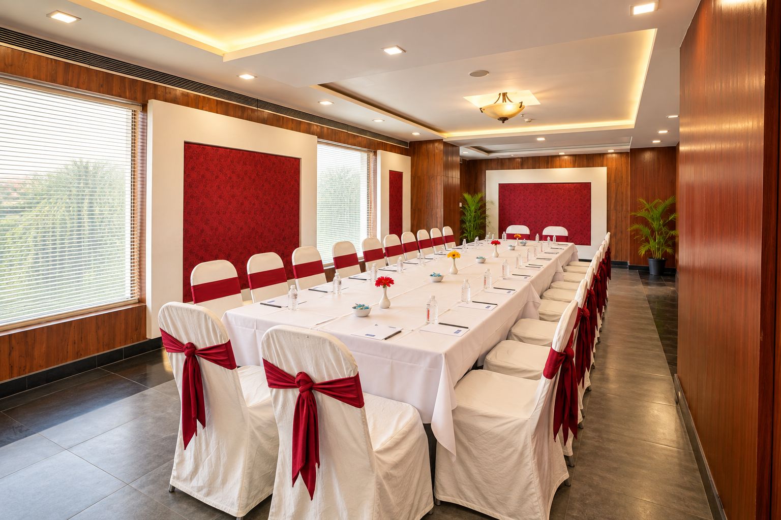 Una sala de conferencias con una mesa larga, sillas blancas con cintas rojas y una pared de acento roja.