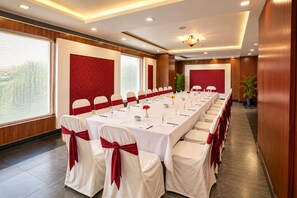 A conference room with a long table, white chairs with red sashes, and a red accent wall. - The Altruist Hitech Hotel (Hyderabad)