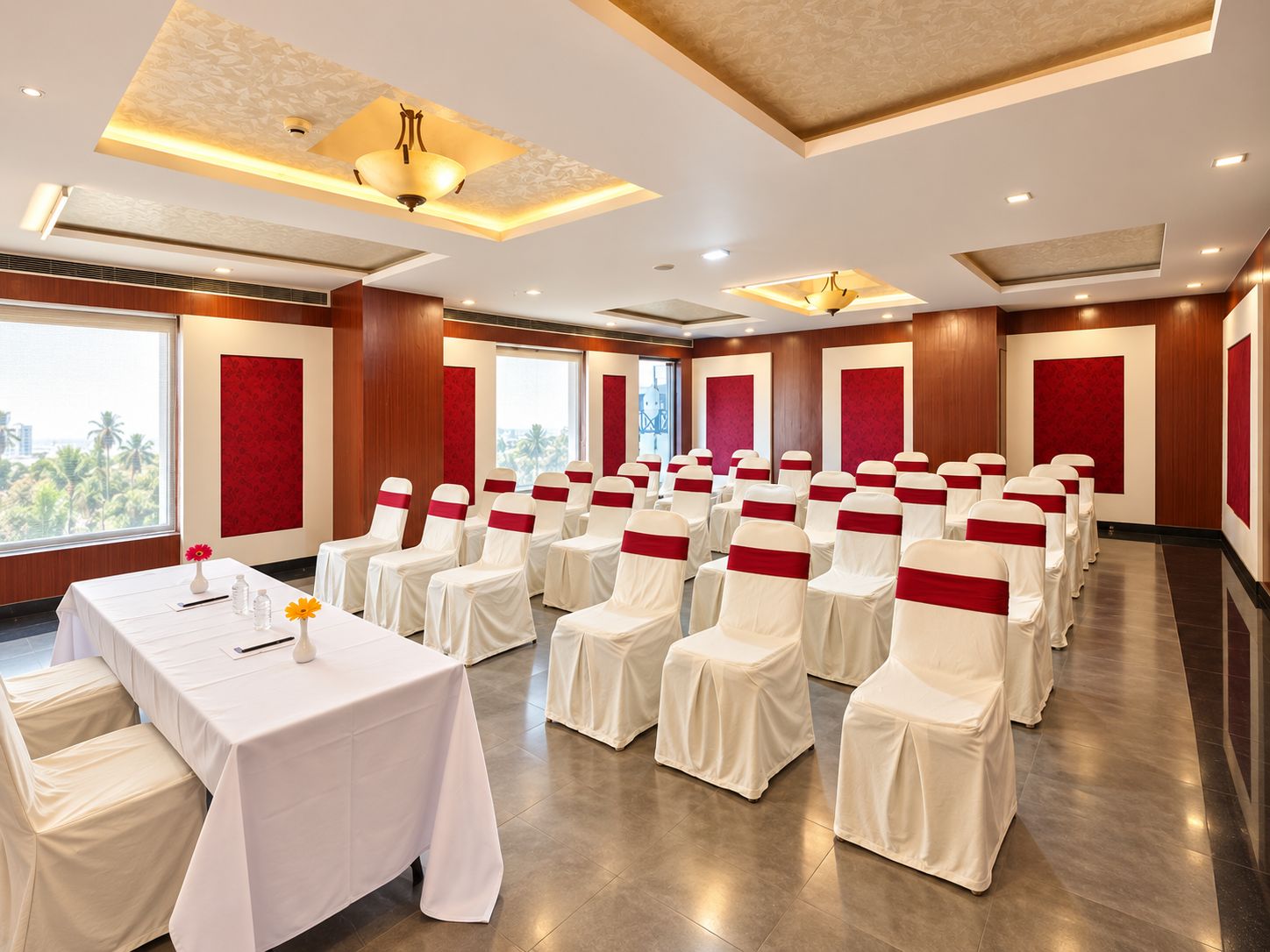 A conference room with rows of chairs, a table with a white tablecloth, and red sashes.