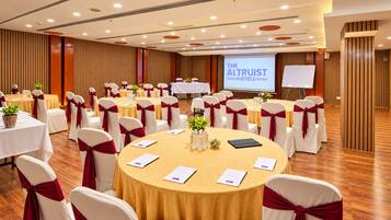 A conference room with round tables, white chairs with red sashes, and a projection screen displaying 'THE ALTRUIST HOTELS'.