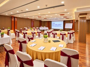 Une salle de conférence avec des tables rondes, des chaises blanches ornées de rubans rouges et un écran de projection affichant le texte « THE ALTRUIST HOTELS ».
