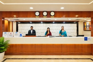 Un comptoir d’accueil avec trois employés, des horloges indiquant différents fuseaux horaires et des panneaux indiquant les services offerts et les mesures de sécurité.