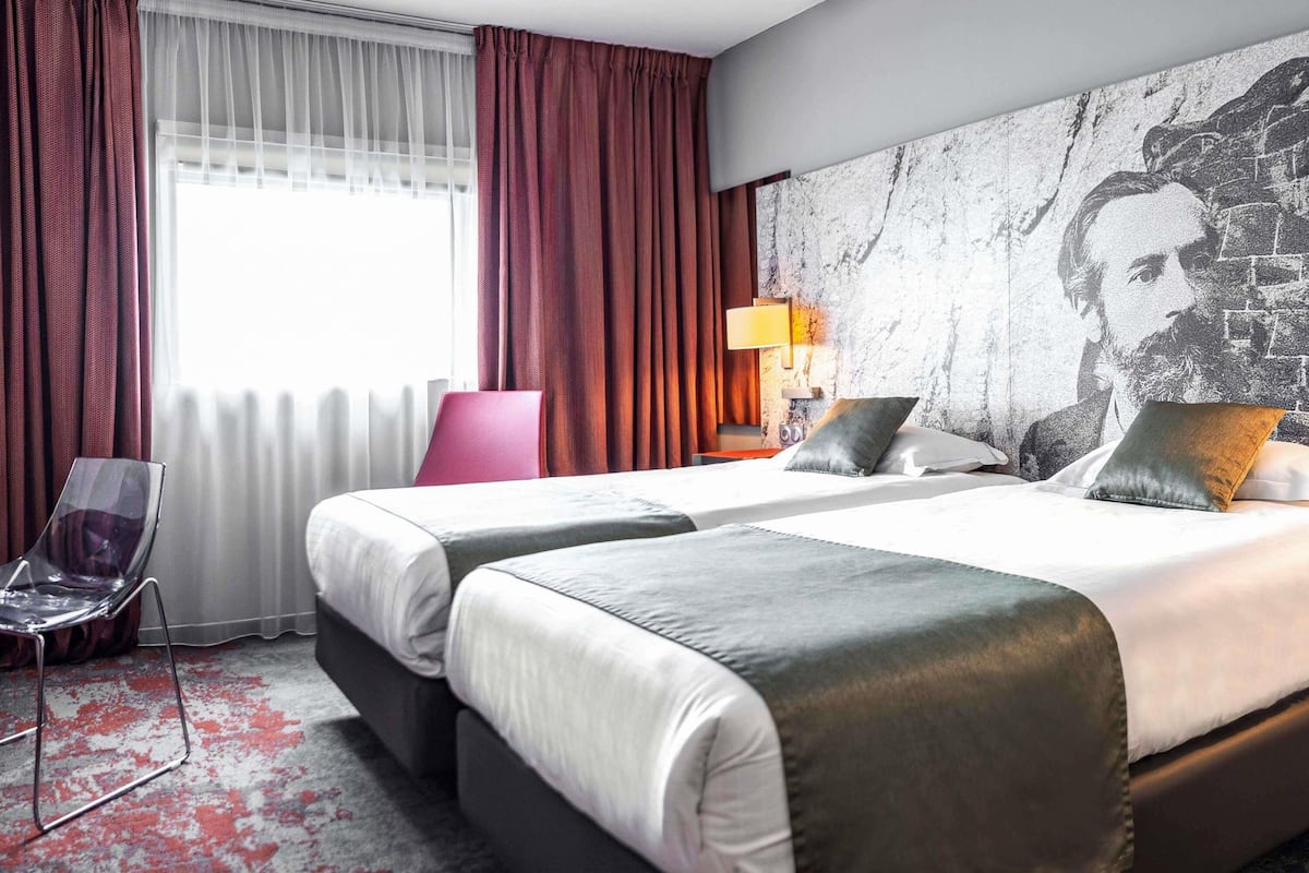 Ein Hotelzimmer mit zwei Betten, einem Sessel, einer Lampe und einem großflächigen Wandbild.