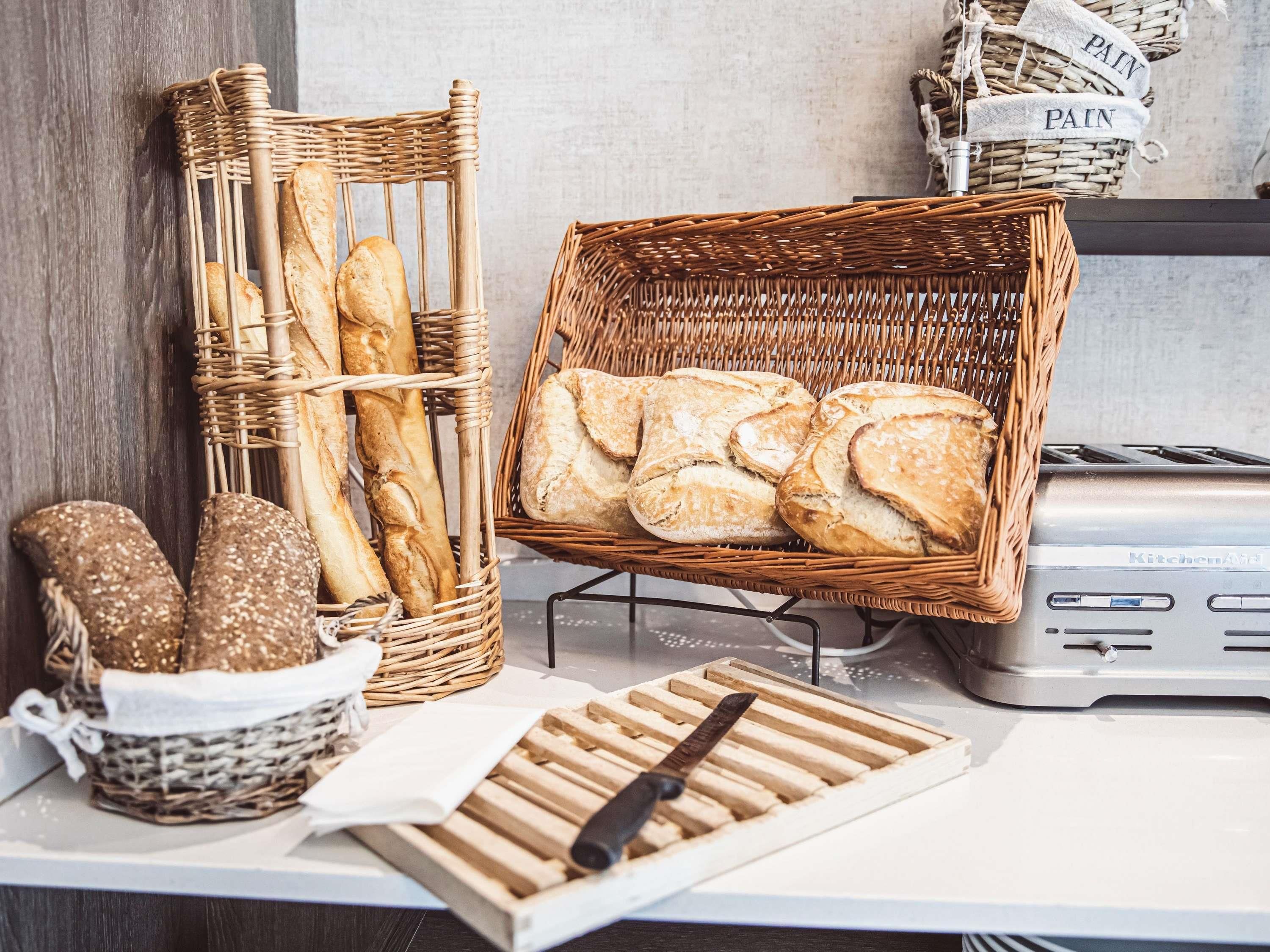 Un plan de travail de cuisine avec un grille-pain, un panier en osier contenant du pain et un autre panier en osier contenant des saucisses.