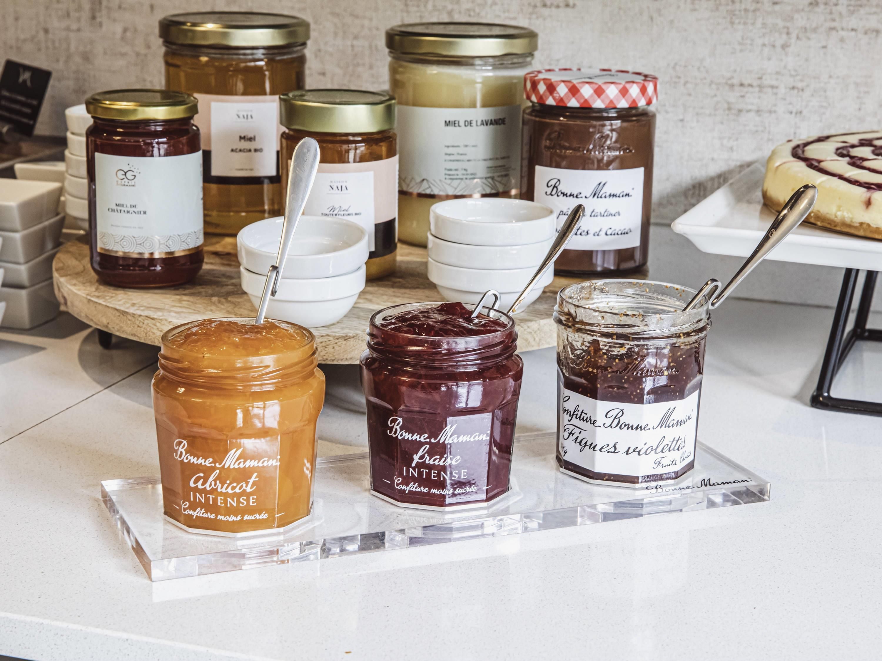 A display of various jars of jam and honey on a marble countertop.