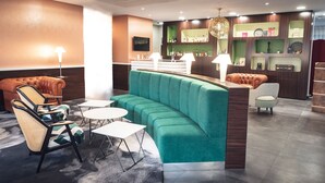 Een moderne lounge met een gebogen groene bank, rieten fauteuils en een bargedeelte met flessen op planken.
