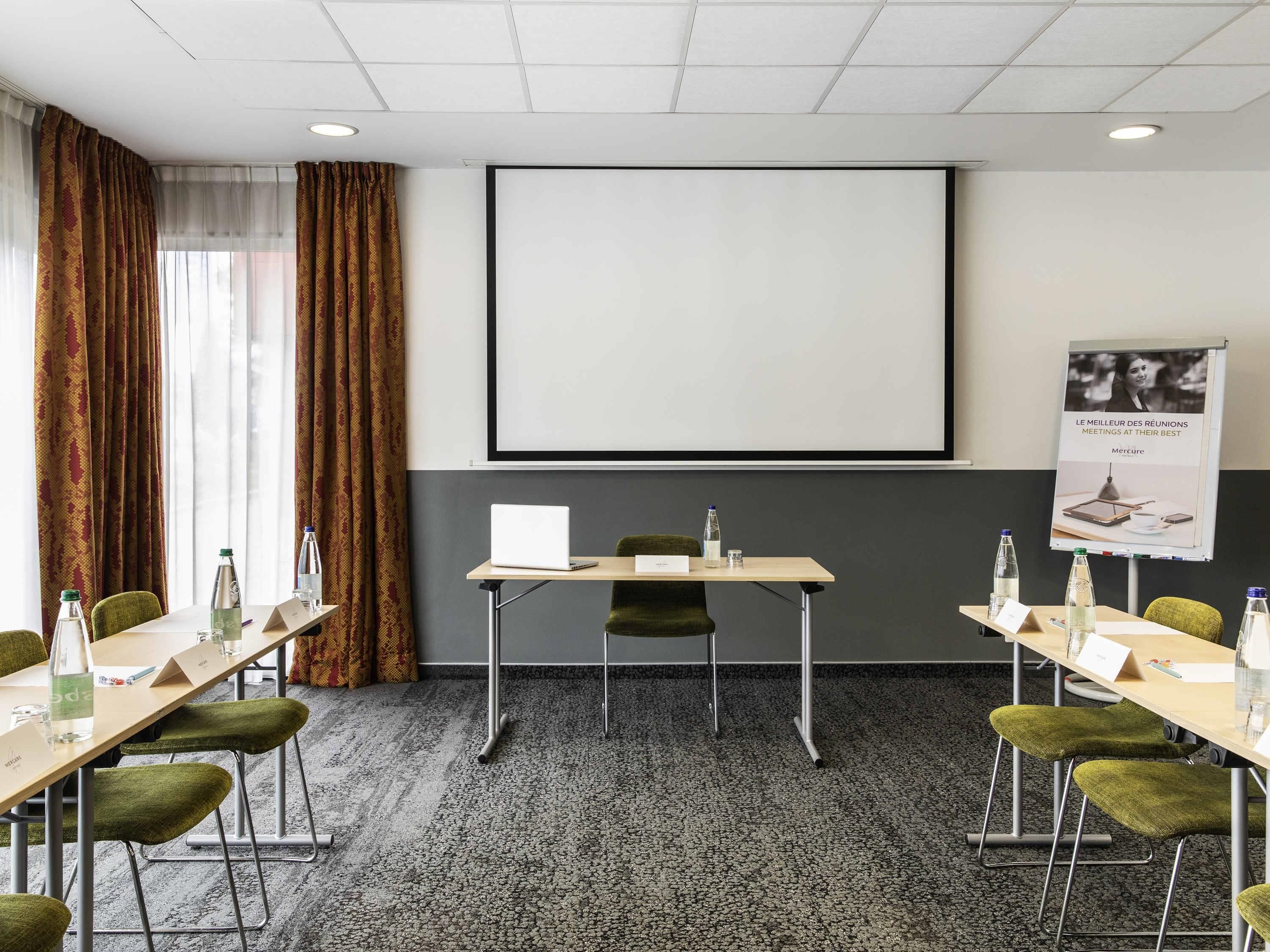 A conference room with a projector screen, tables, chairs, and a water bottle on each table.