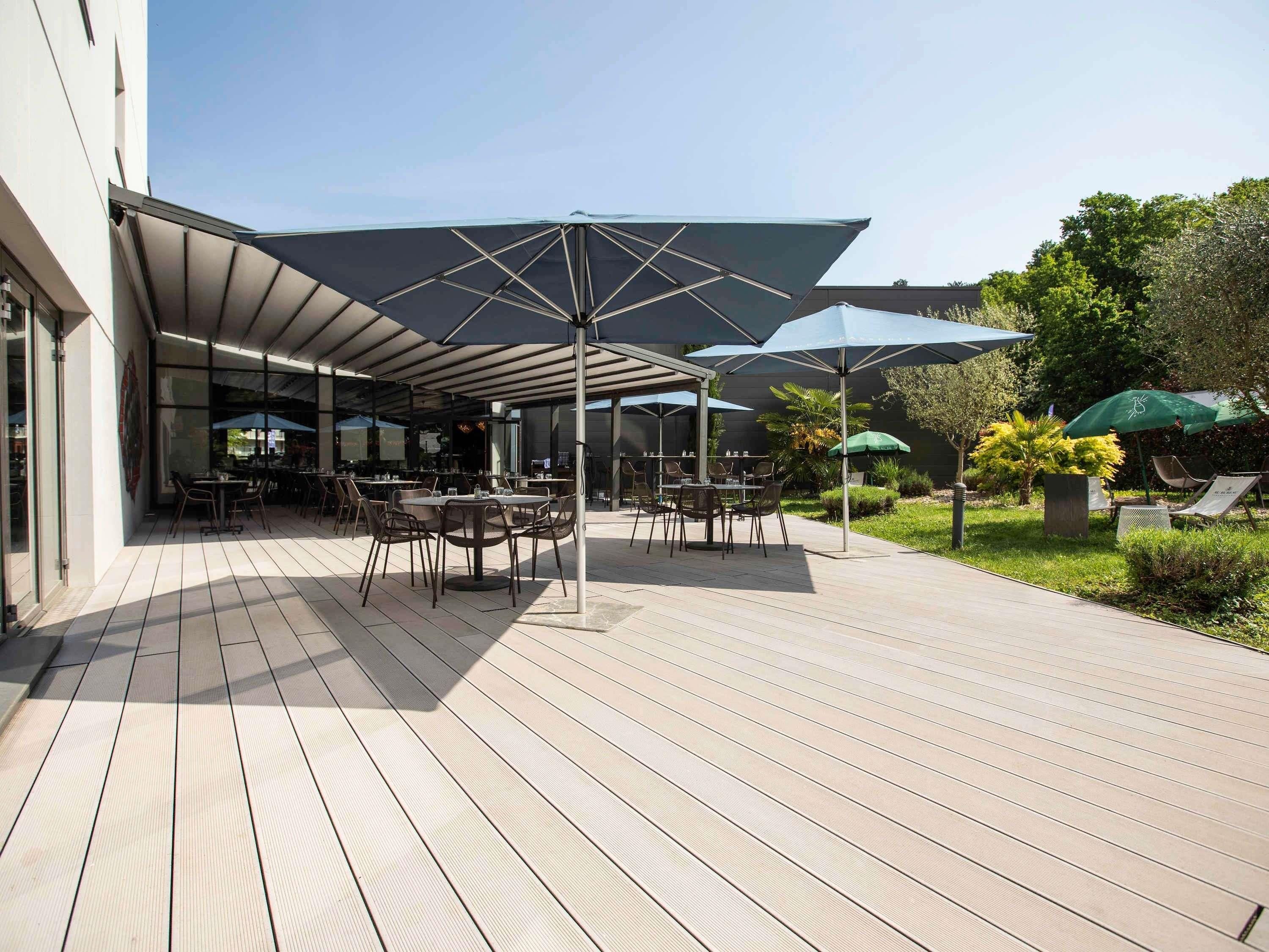 Un espace extérieur aménagé en terrasse, avec des tables, des chaises, des parasols et un jardin.