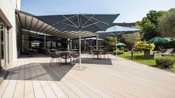 Un espace extérieur aménagé en terrasse, avec des tables, des chaises, des parasols et un jardin.
