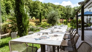 Een terras met tafels voor twee personen, omgeven door weelderige begroeiing en een heldere lucht.