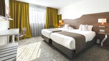 A hotel room with two beds, a desk, a chair, and a large window with curtains.
