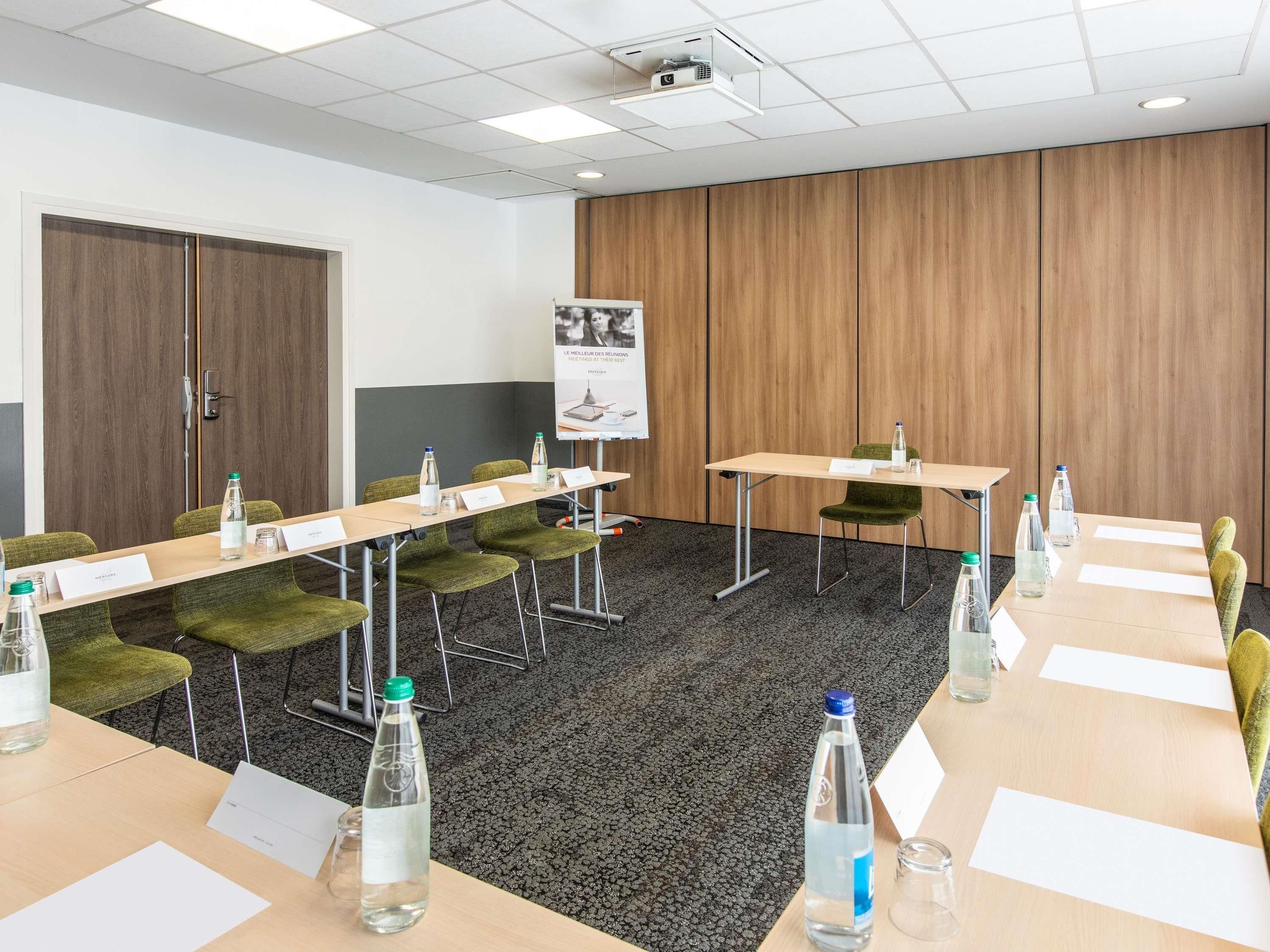 A conference room with a long table, chairs, nameplates, water bottles, and a projector screen.