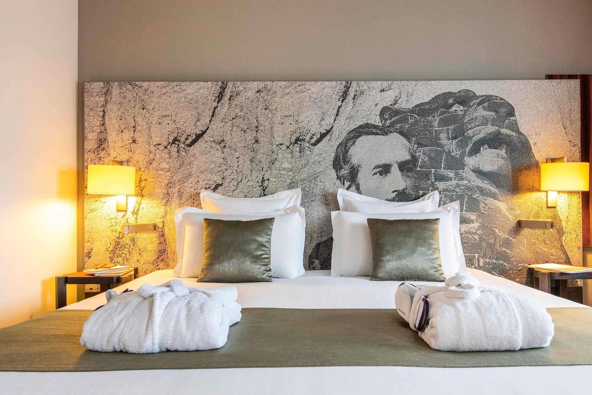 Ein Hotelzimmer mit einem großen Bett, zwei Nachttischen, Lampen und einer strukturierten Wand.