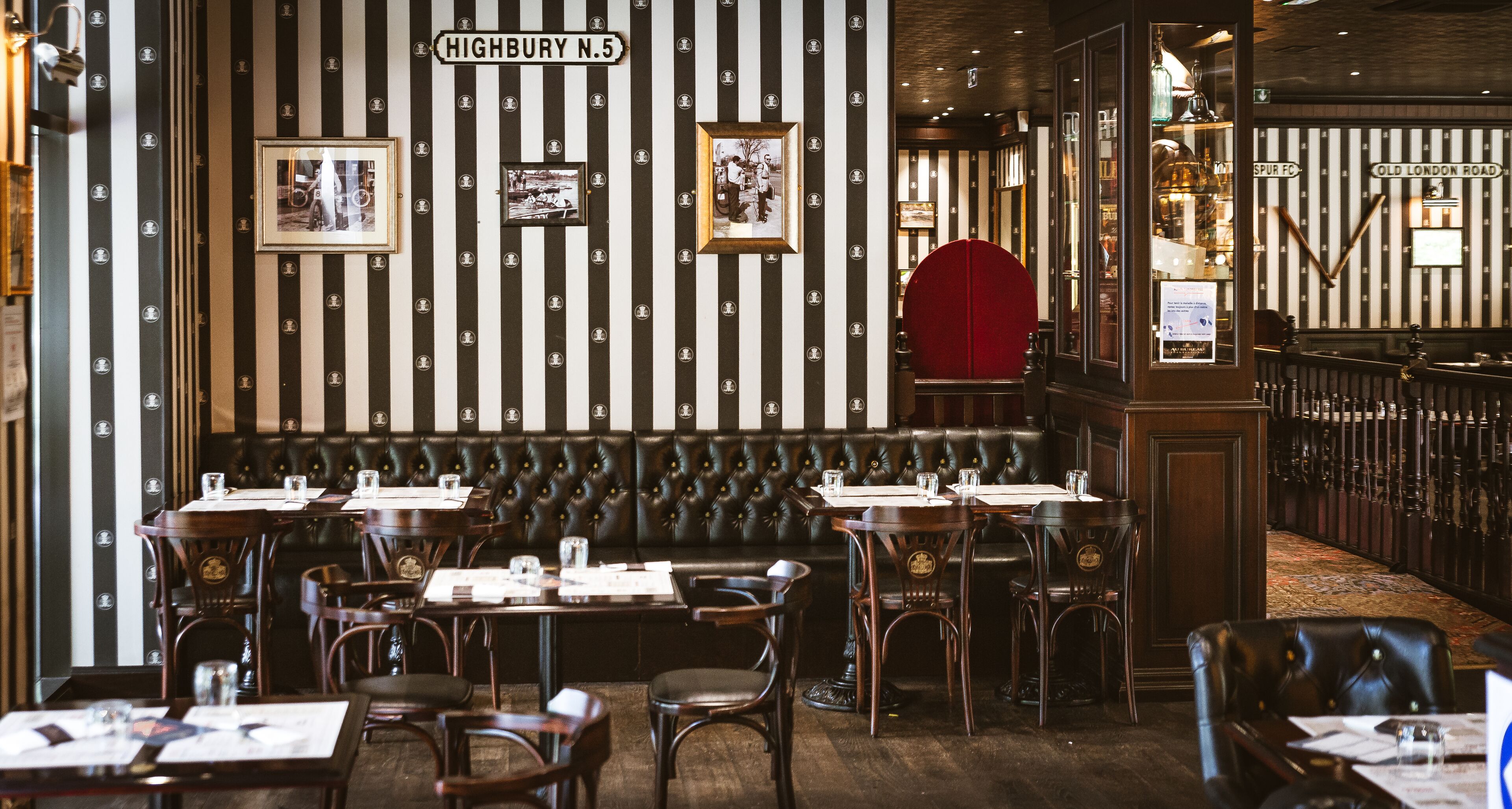 A restaurant interior with striped wallpaper, leather booths, wooden tables, and framed pictures on the wall.