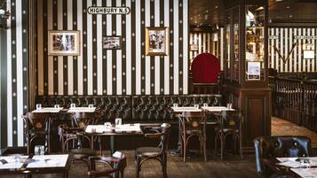 A restaurant interior with striped wallpaper, leather booths, wooden tables, and framed pictures on the wall.