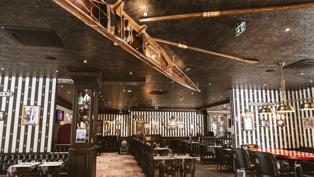 A restaurant interior with striped walls, wooden furniture, and a hanging wooden structure. - Mercure Belfort Centre (Belfort)