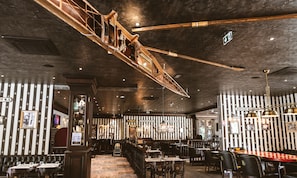A restaurant interior with striped walls, wooden furniture, and a hanging wooden structure.