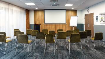 A conference room with a carpeted floor, a podium, a whiteboard, and a projector screen.