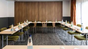 A conference room with a long table, green chairs, nameplates, water bottles, and a projector on the ceiling.