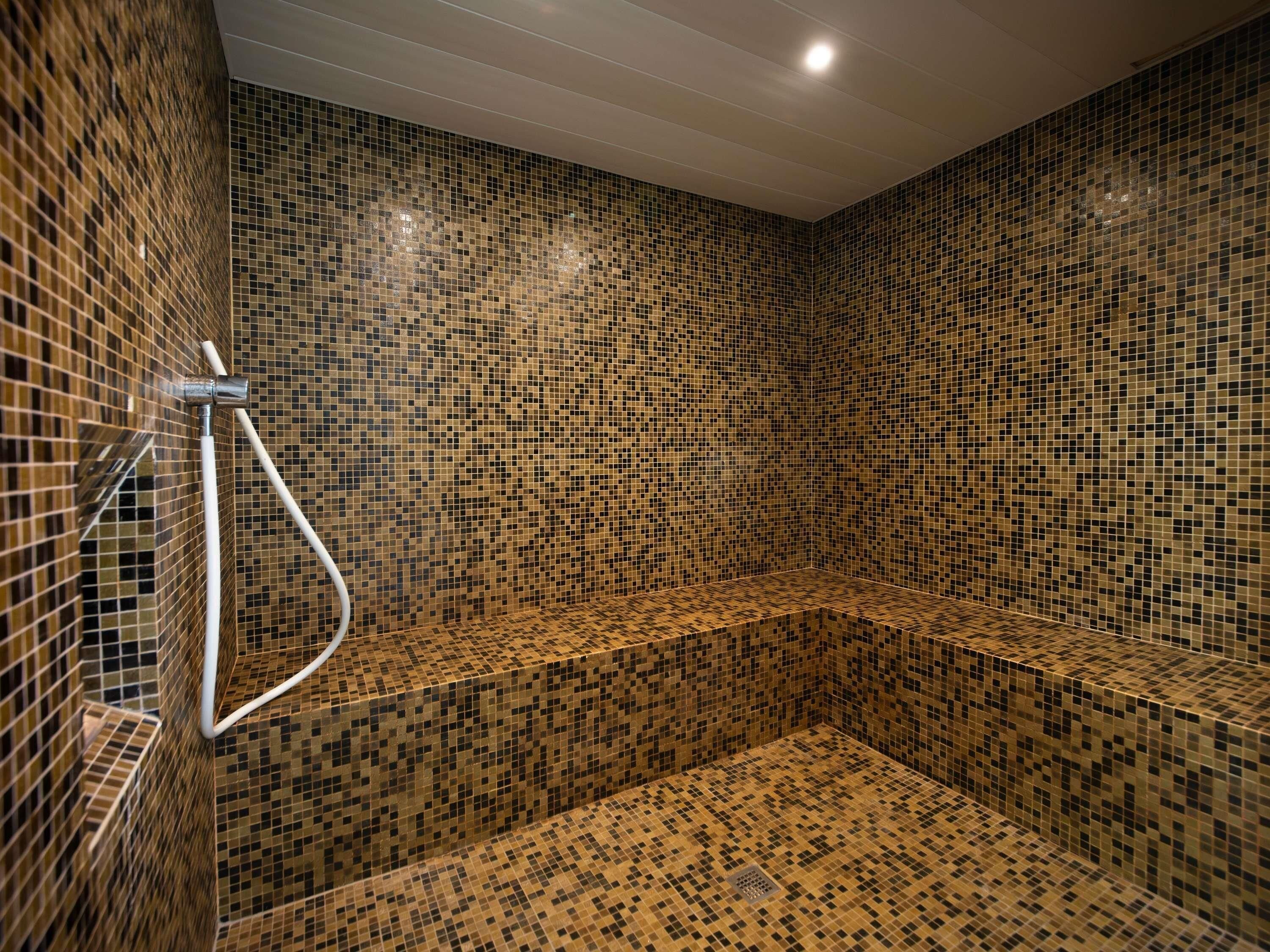 Zona de ducha con paredes de azulejos de mosaico y un cabezal de ducha de metal.